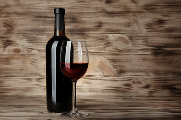 Bottle and glass with red wine on wooden background