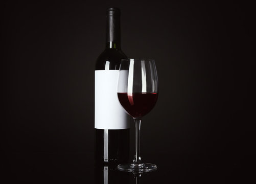 Glass of red wine and bottle with blank label on black background. Mock up for design