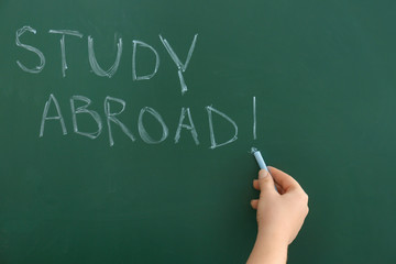 Woman writing phrase "Study abroad" on chalkboard