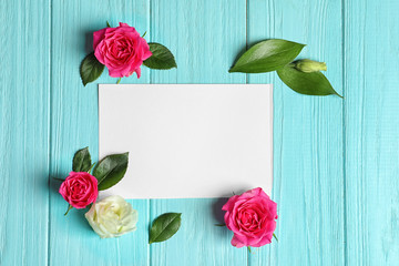 Beautiful roses and empty card on wooden background
