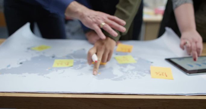 4K Diverse business team looking at world map, using tablet & brainstorming with sticky notes. Slow motion.