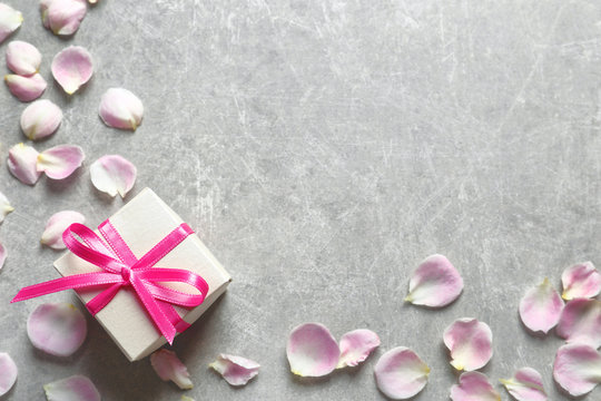 Gift box and petals on grey background