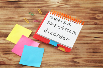Notepad with text AUTISM SPECTRUM DISORDER on wooden background
