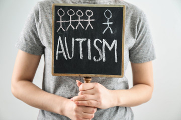 Woman holding blackboard with word AUTISM  on light background