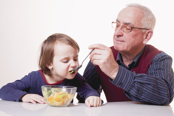 Grandpa feeding his grandchild with fruits salad. (Healthy foods, vitamins, love, generation, relationship concept)