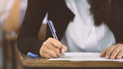 Close up to hand of student  holding pen and taking exam in classroom with stress for education test.