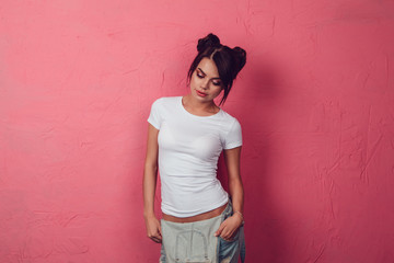 Attractive woman in a white t-shirt stands on a pink background. Mock-up.
