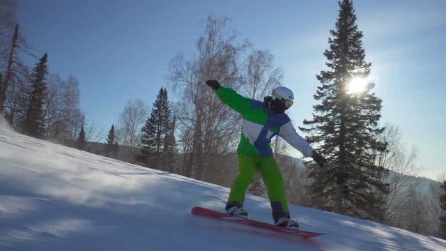 Sportsman in bright green clothes is jumping on snowboard upon a slope of the hill at sunny winter day