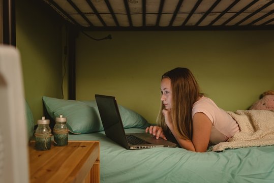 Girl lying on bunk bed using her laptop in bedroom