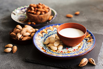 Almond milk in a clay pot and fresh nuts over dark slate background, selective focus. Dairy-free, vegan healthy food concept