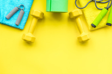 Fitness background. Equipment for gym and home. Jump rope, dumbbells, expander, mat, water on pastel yellow background top view space for text