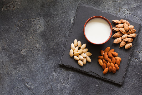 Almond milk in a clay pot and fresh nuts over dark slate background, selective focus. Dairy-free, vegan healthy food concept