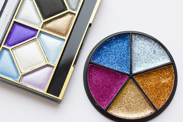 Make Up Beauty Fashion Concept. Daily and evening shimmer eye shadow palette and bright glitter round palette on white, top view