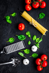 Italian pasta concept. Spaghetti, tomatoes, garlic, cheese grater, spoon for spaghetti on black background top view