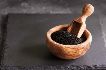 Black cumin or nigella sativa or kalonji seeds in bowl with spoon on black slate background,...