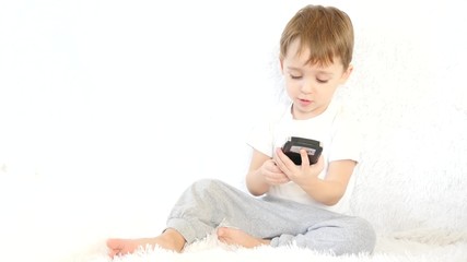 A child is sitting on a white sofa, playing with a smartphone and smiling. Motion camera slider.