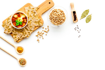 Middle Eastern cuisine. Bowl with hummus among pieces of crispbread and spices on white background top view copy space