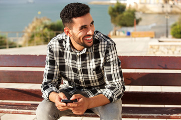 Obraz premium young arabic man smiling outside with mobile phone