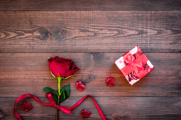 Prepare the prsesnts or surprise for Valentine's day. Red gift box near red rose on dark wooden background top view space for text