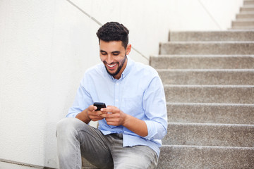 young arabic man sitting on steps and looking at mobile phon