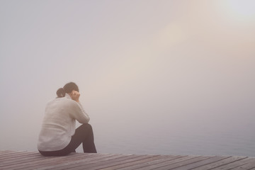 Anonyme traurige Frau sitzt am See im Nebel