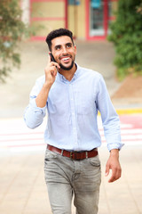 smiling young arabic man walking on the street and talking on cellphone