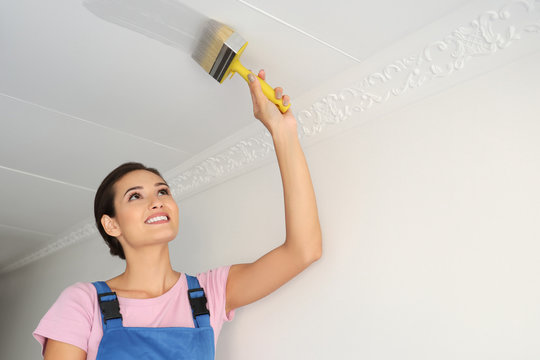 Decorator painting white ceiling with brush in room
