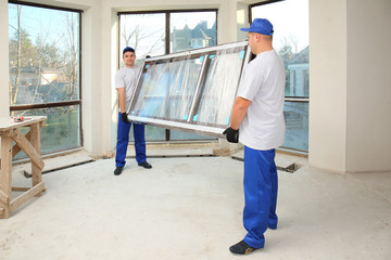 Construction workers carrying window glass indoors