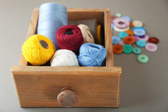 Wooden drawer with sewing threads and crocheting clews on grey background