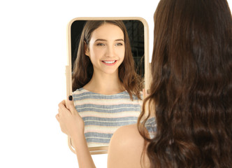 Young pretty girl looking in mirror on white background