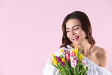 Beautiful woman holding bouquet of tulips on color background