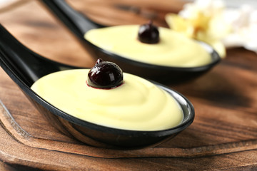 Spoon with tasty vanilla pudding on wooden board, closeup