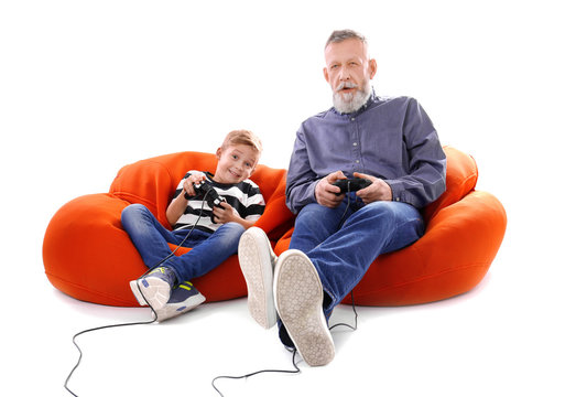 Cute boy with grandfather playing video game on white background