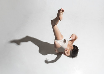 Young beautiful dancer in beige dress dancing on gray background