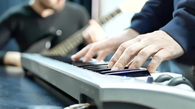 Rock band practice play piano. Musician hands playing on electric piano with guitar player. Music band concert. Man lead guitarist playing electrical guitar on background