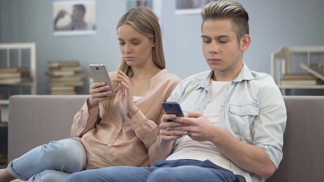 Couple in love indifferently sitting on couch looking at their smartphones