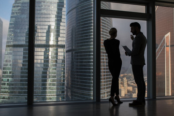 Fototapeta na wymiar Business people talking negotiating standing near large panoramic window with big city buildings.