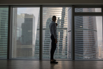 Businessman standing near large panoramic window with big city buildings.