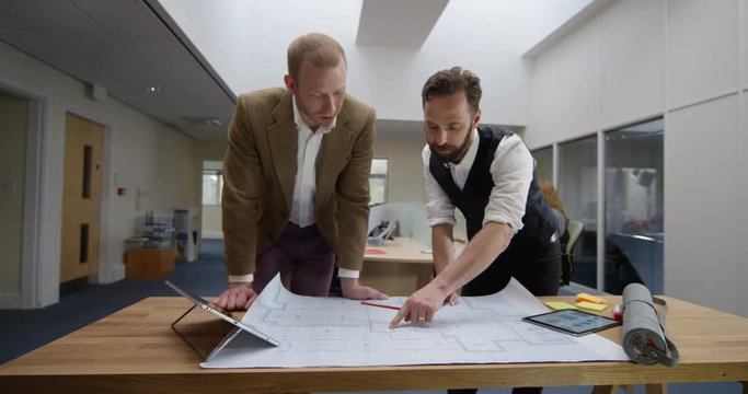 4K 2 Architects in a planning meeting with their colleagues working in background. Slow motion.