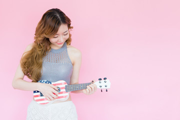Young Asian Woman Playing Ukulele isolated on pink background with copy space