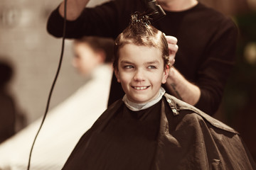 Handsome boy getting his hair and beard cut at barber shop