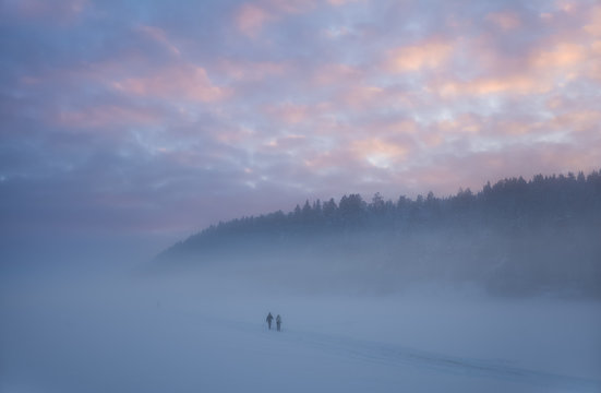 Two skiers coming out of the mist in the forests after sunset. Oslo, Norway