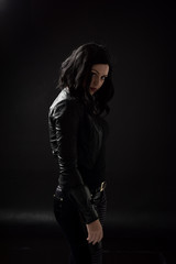 portrait of black haired girl wearing leather clothes, moody lighting on black background.
