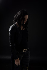 Fototapeta na wymiar portrait of black haired girl wearing leather clothes, moody lighting on black background.