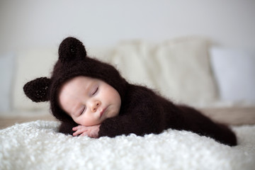 Sweet little baby boy, dressed in handmade knitted brown soft teddy bear overall, sleeping cozy