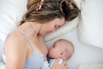 Young mother breastfeeds her baby, holding him in her arms and smiling