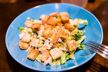 Macro closeup of homemade ceasar salad on blue plate, wooden table, fork, croutons, lettuce