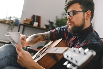 Young guitarist hipster at home with guitar sitting writing melody inspired