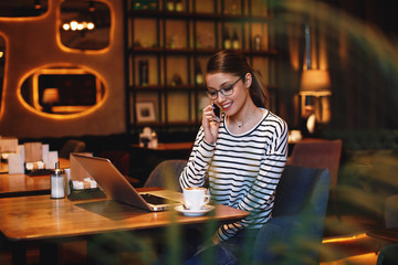 Young women talking on the phone with laptop on the table in front of her
