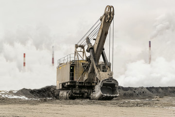 Heavy bucket mining excavator on a crawler track against a background of dense factory strong smog...
